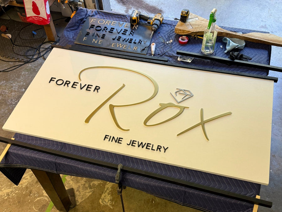 Forever Rox sign face with letters placed on a shop table beside the frame pieces and letter offcuts