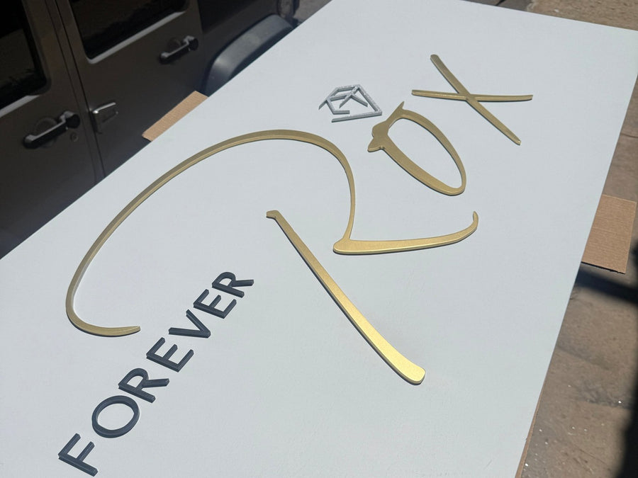 Gold script and dark letters laid out on the white Forever Rox sign face