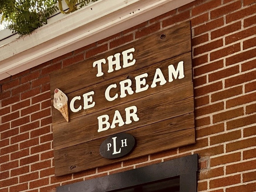 The Ice Cream Bar sign in white letters on barn wood, with an ice cream cone as the letter I and the PLH logo, above a walk-up window